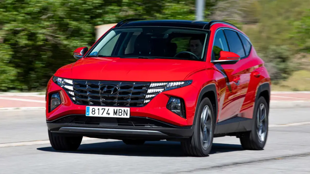 Un conductor prueba el Hyundai Tucson híbrido enchufable rojo, con su distintiva parrilla y luces LED, circulando por una carretera.