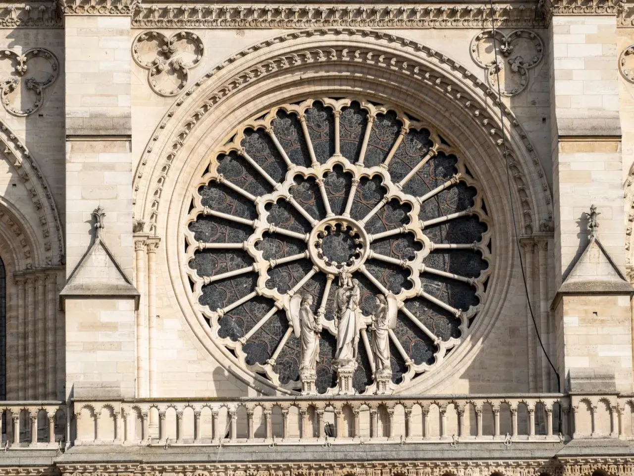 Ein Rosettenfenster im Stil der Gotik-Kunst, umrahmt von Steinfiguren und filigranen Verzierungen an einer Kathedrale.