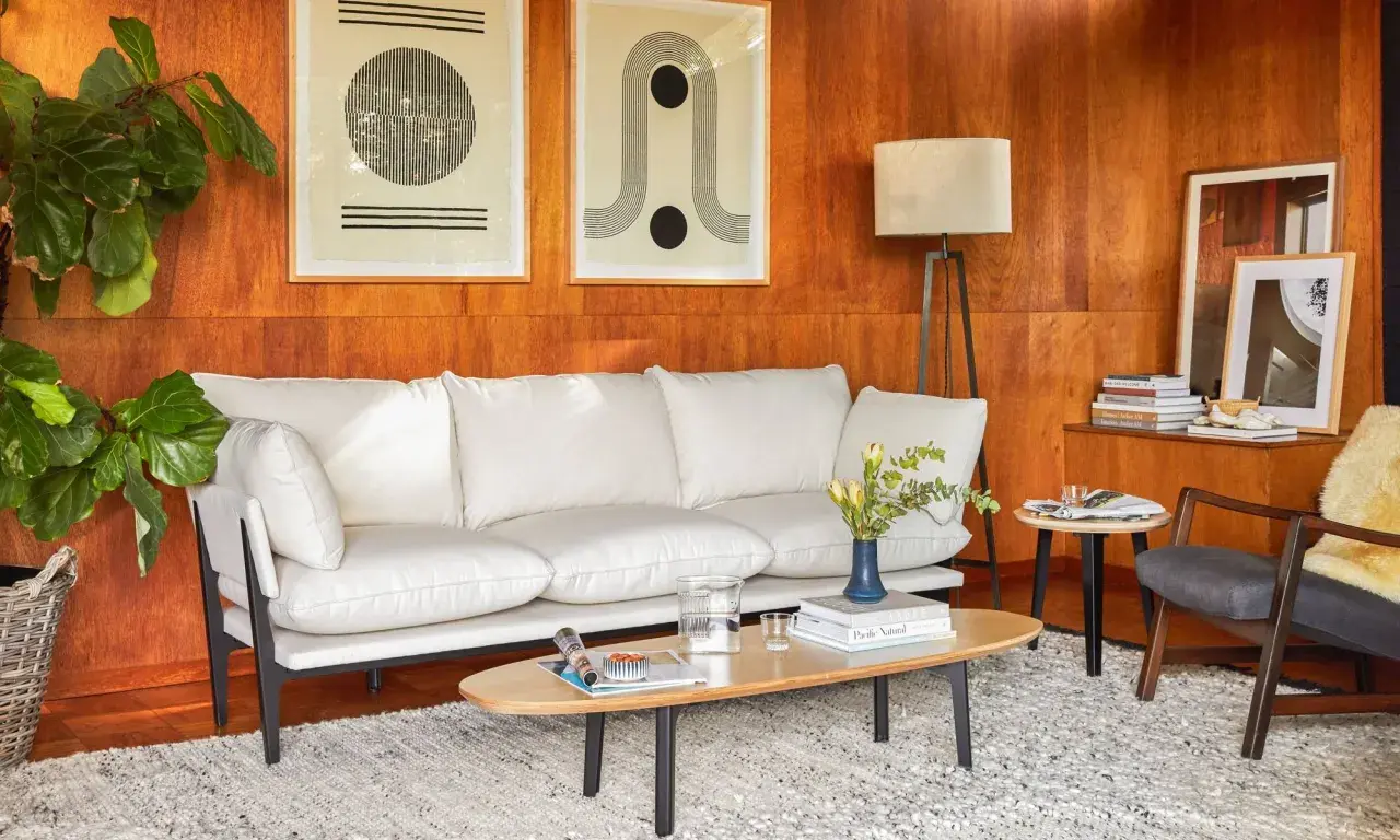 A modern living room with a white sofa, art, and a floor lamp, all set against warm wood tones.