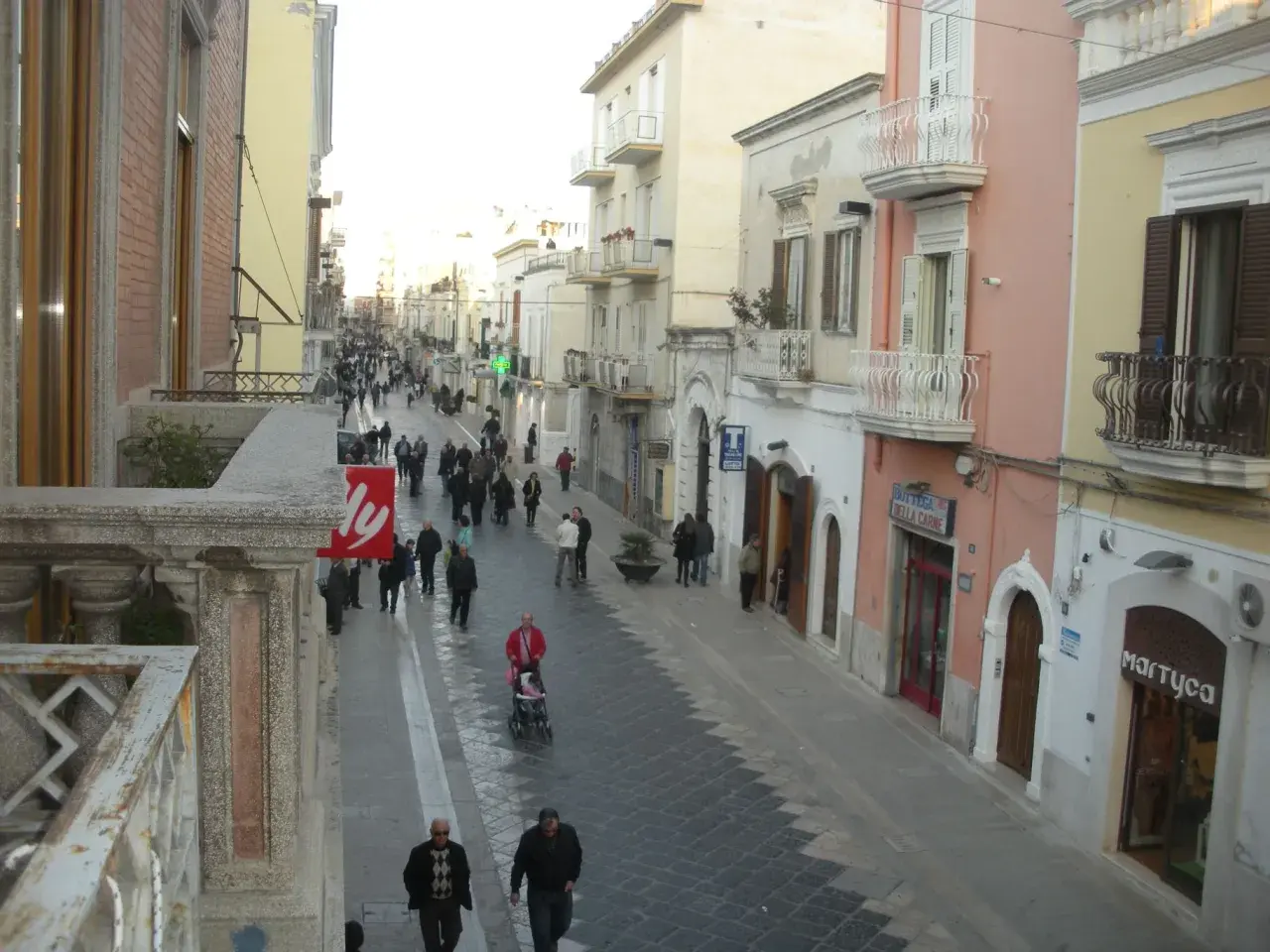 Passeggiata serale per gli abitanti di Manfredonia in una via commerciale animata, con negozi e palazzi storici.