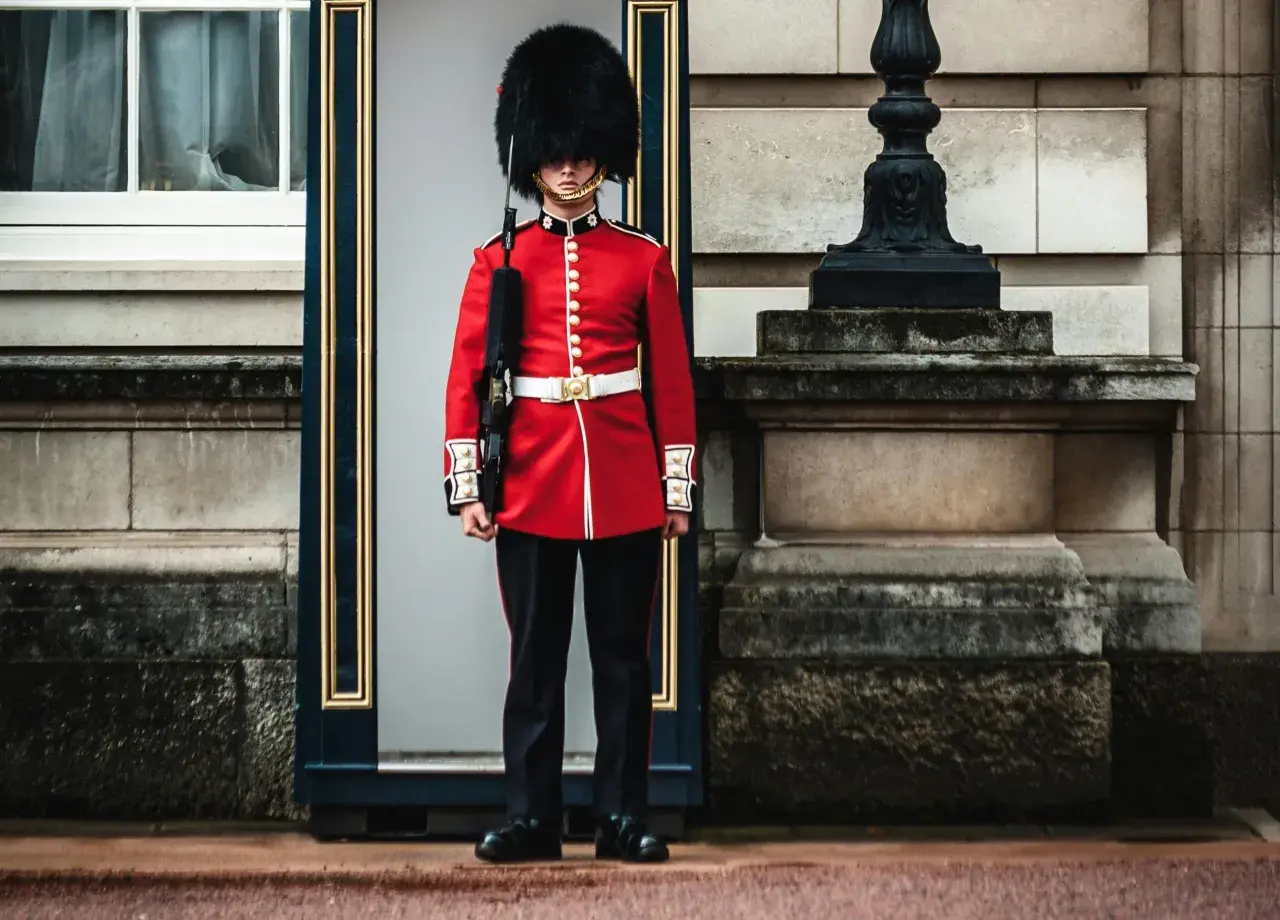 Un guardia con uniforme rojo y sombrero de piel, un típico inglés, vigila la entrada de un edificio histórico.