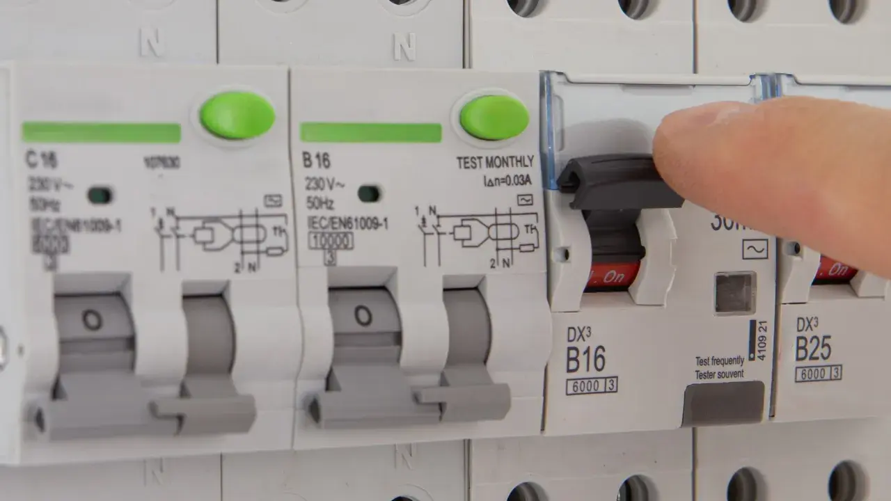 Dłoń naciska dźwignię wyłącznika, który jest częścią instalacji elektrycznej. Czy różnicówka jest obowiązkowa? To pytanie o bezpieczeństwo.