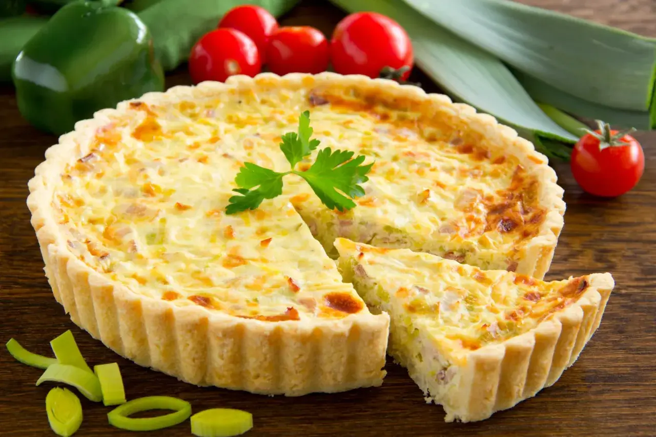 Quiche Lorraine con pasta sfoglia, un classico della cucina francese, con una fetta tagliata per mostrare il ripieno cremoso e saporito.