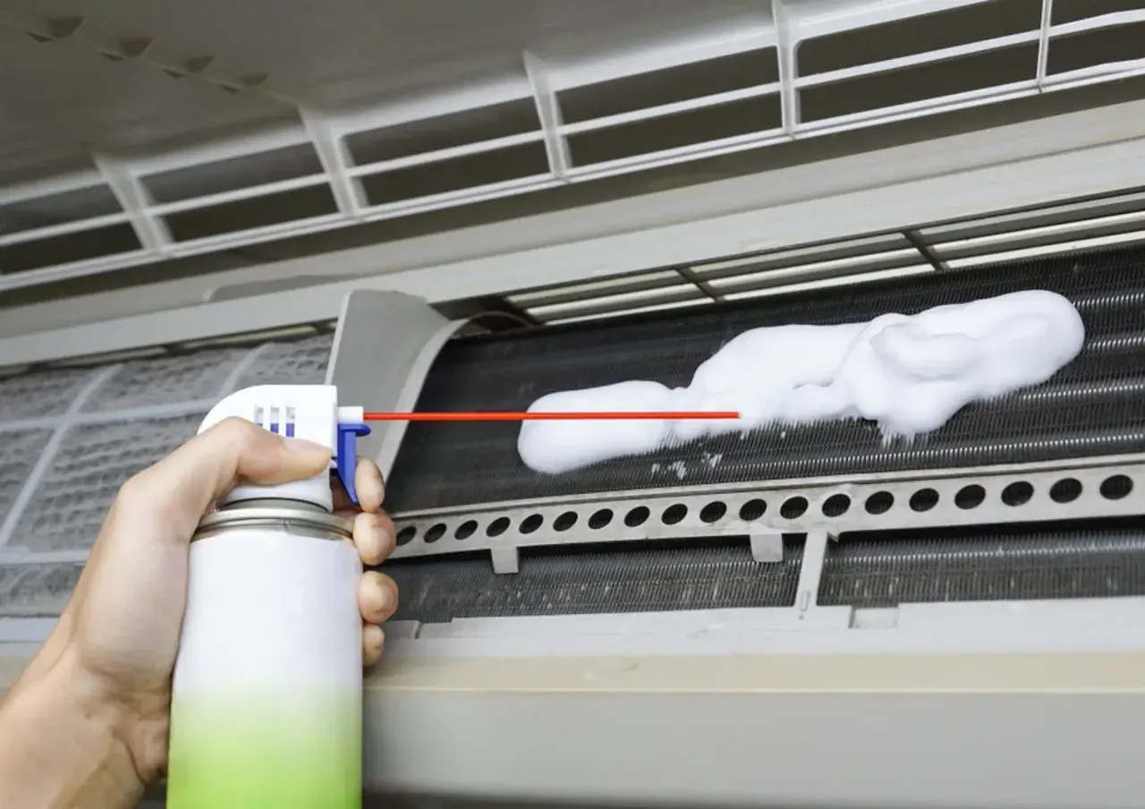 Mano rociando espuma limpiadora en las aletas de un aire acondicionado para limpiar bandeja aire acondicionado.
