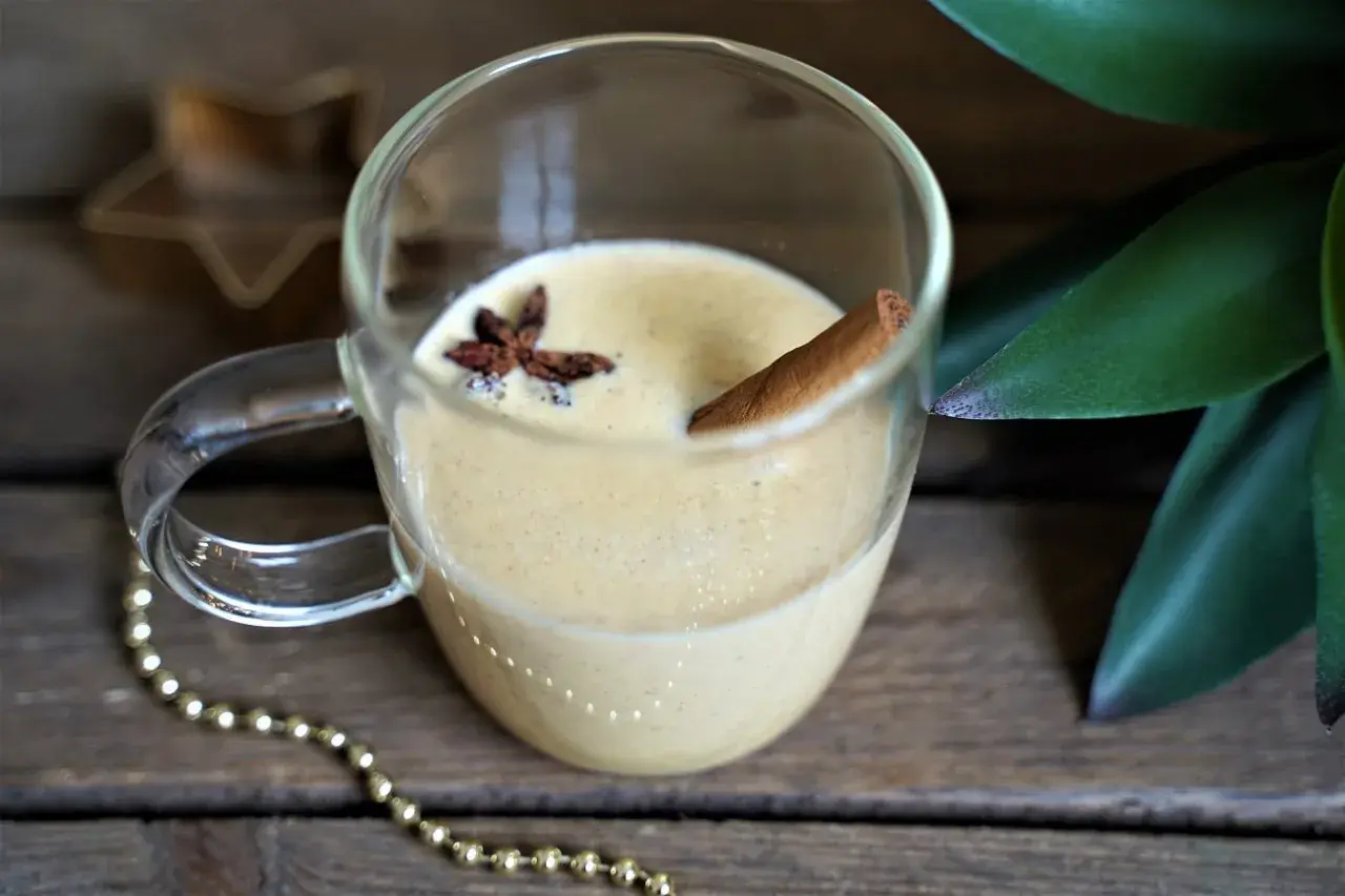 Un verre de lait de poule crémeux, garni d'anis étoilé et d'un bâton de cannelle, sur fond de bois rustique.