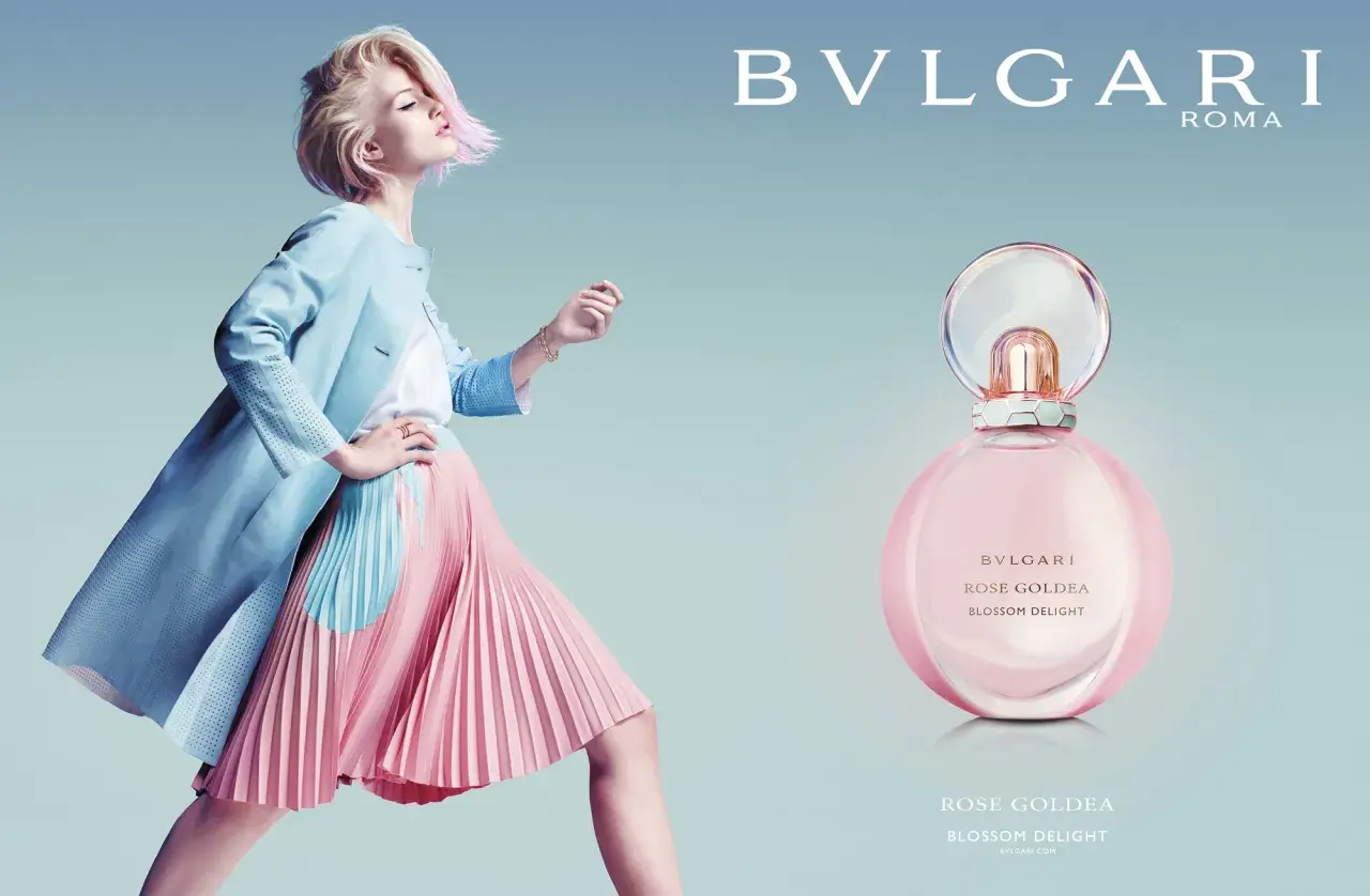 Kobieta w pastelowej stylizacji obok flakonu perfum Bvlgari Rose Goldea Blossom Delight.