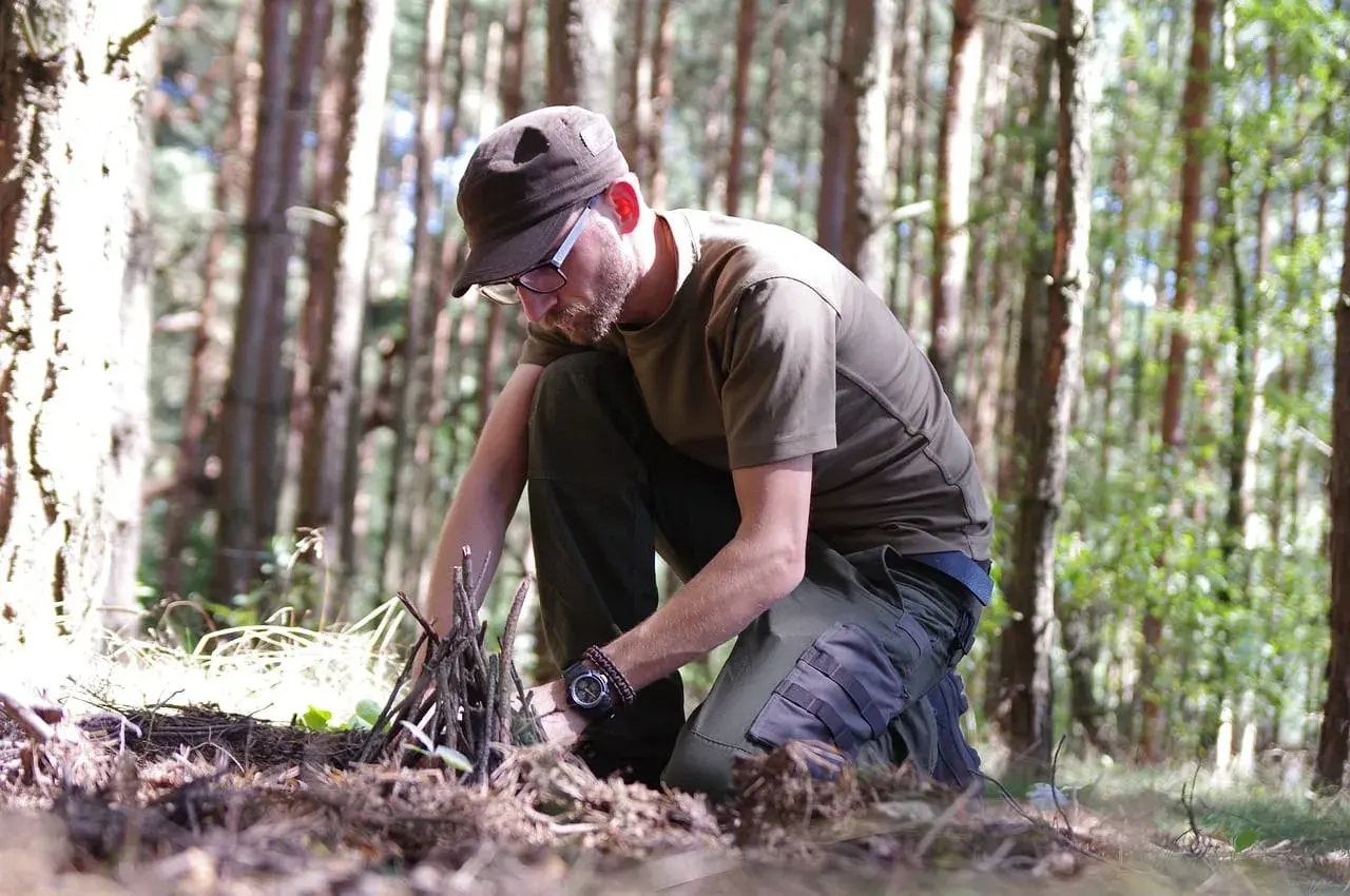 Mężczyzna w lesie przygotowuje rozpałkę. To pokazuje, survival co to znaczy: umiejętność radzenia sobie w trudnych warunkach.
