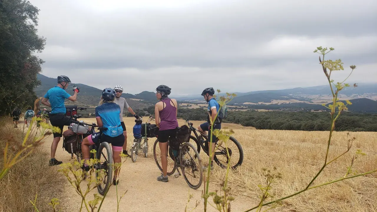 Ciclistas en ruta por la EuroVelo 6, disfrutando del paisaje rural y las colinas bajo un cielo nublado.