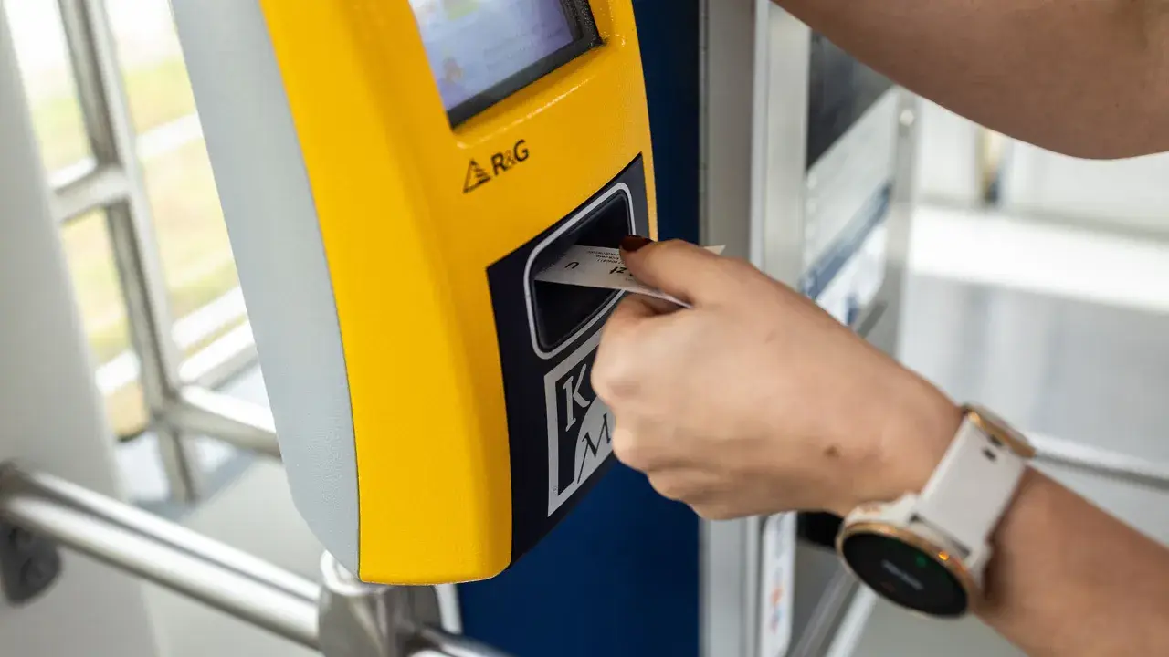 Ręka z zegarkiem wkłada bilet godzinny Kraków do żółtego automatu.