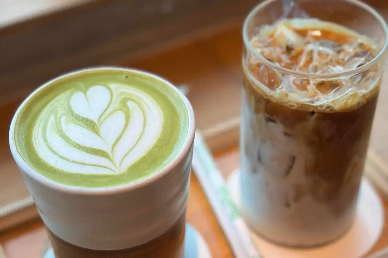 Grüner Matcha Latte mit Herz-Muster neben einem Eiskaffee. Der Matcha Mate Unterschied wird hier visuell dargestellt.