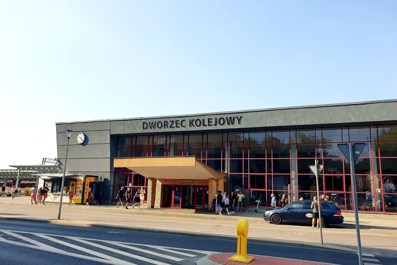 Dworzec kolejowy w Krakowie, z ludźmi i samochodami przed wejściem.