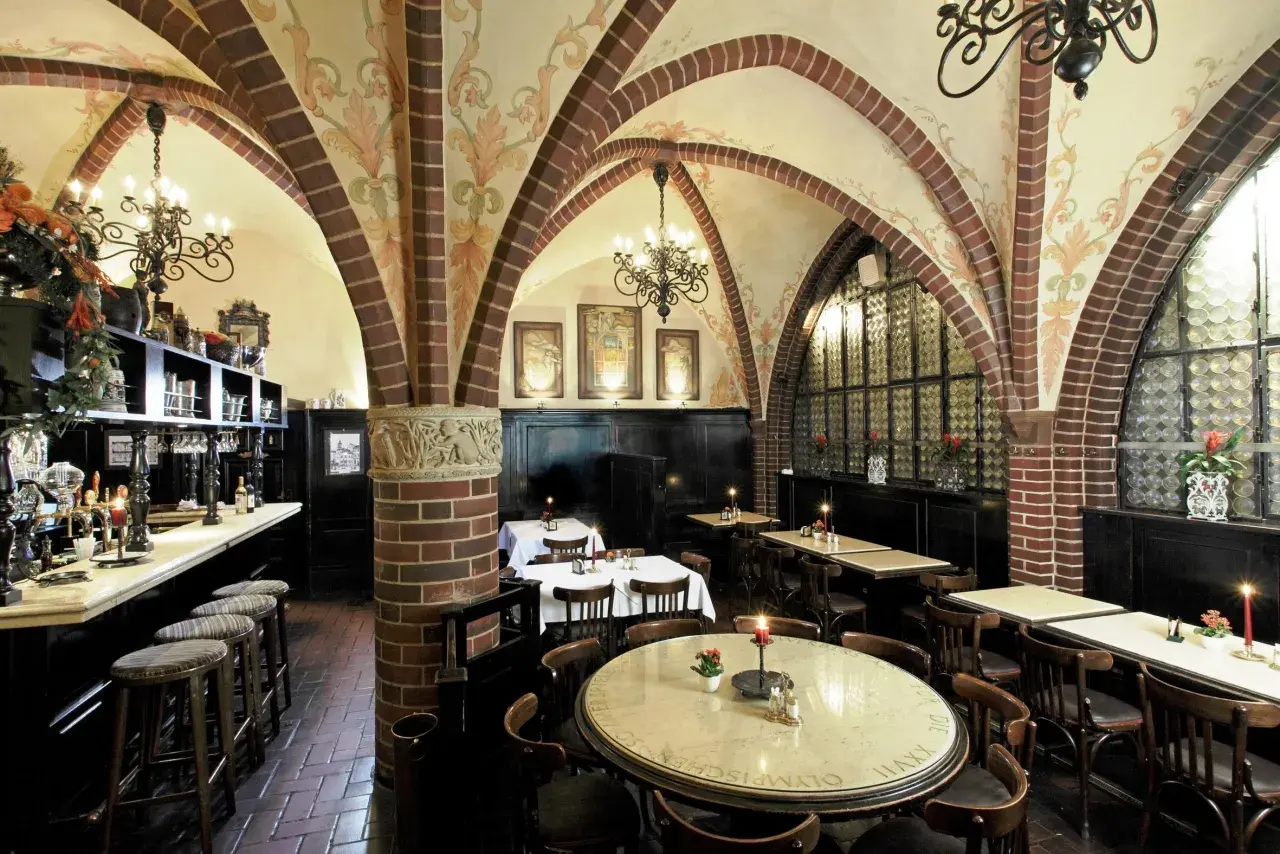 Gemütliche Atmosphäre in einem Berliner Restaurant mit Gewölbedecke, Kronleuchtern und Holztischen.