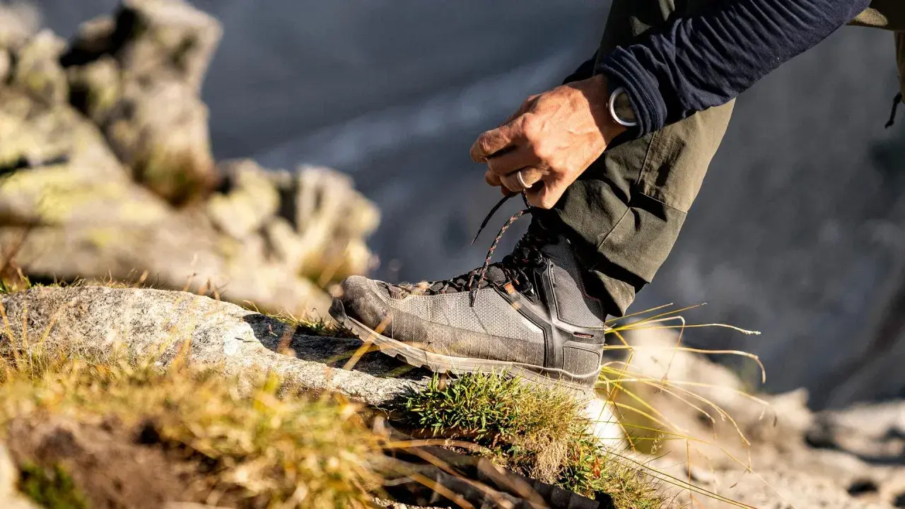 Mężczyzna sznuruje buty trekkingowe na kamieniu. Czy buty trekkingowe powinny być większe? Odpowiedź tkwi w komforcie i ochronie palców.
