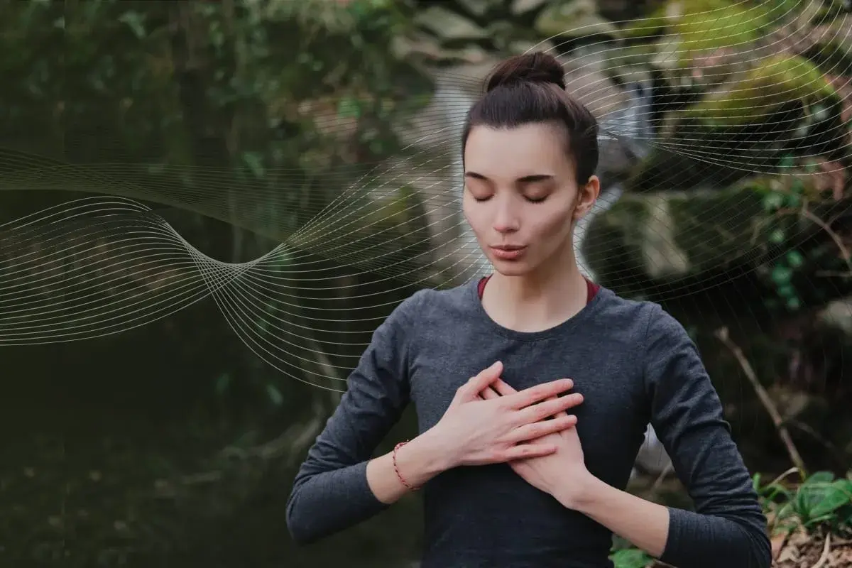 Kobieta z zamkniętymi oczami praktykuje techniki oddychania pranayama na tle natury.