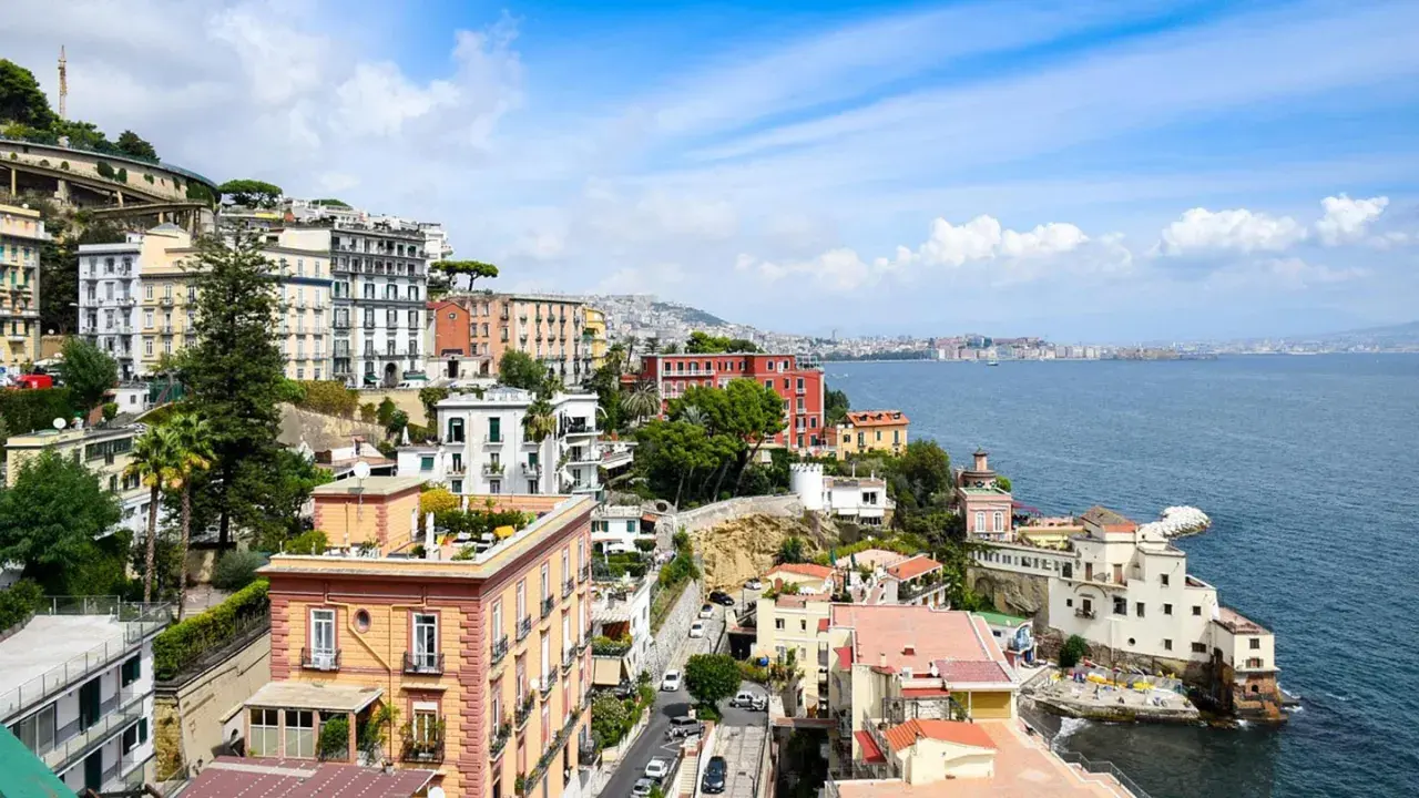 Färgstarka hus klättrar uppför sluttningen vid Neapel, Italien, med havet glittrande i bakgrunden.