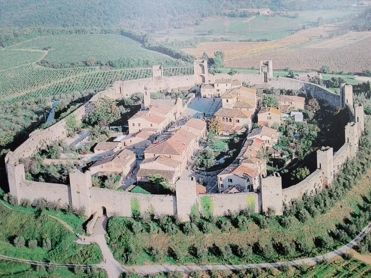 Vista aerea di Monteriggioni, un borgo medievale fortificato in Toscana, con le sue mura intatte e le torri che si stagliano sul paesaggio collinare.