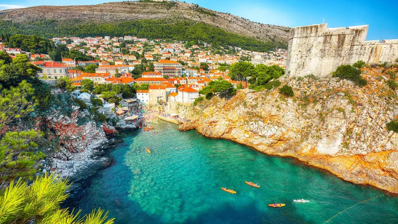 Kajaker på tur i det turkosa vattnet vid Gamla stan Dubrovnik, med klippor och stadens takåsar i bakgrunden.