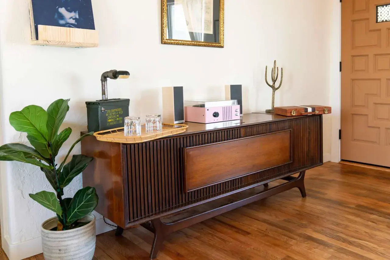 A mid-century modern wood console with a record player, speakers, and a fiddle leaf fig plant.