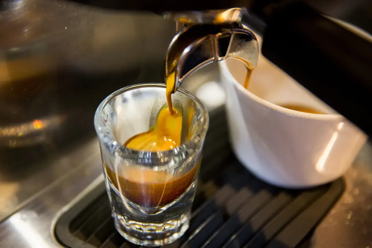 Gorący strumień kawy spływa do szklanki, tworząc idealne espresso. To właśnie taka kawa jest najlepsza!
