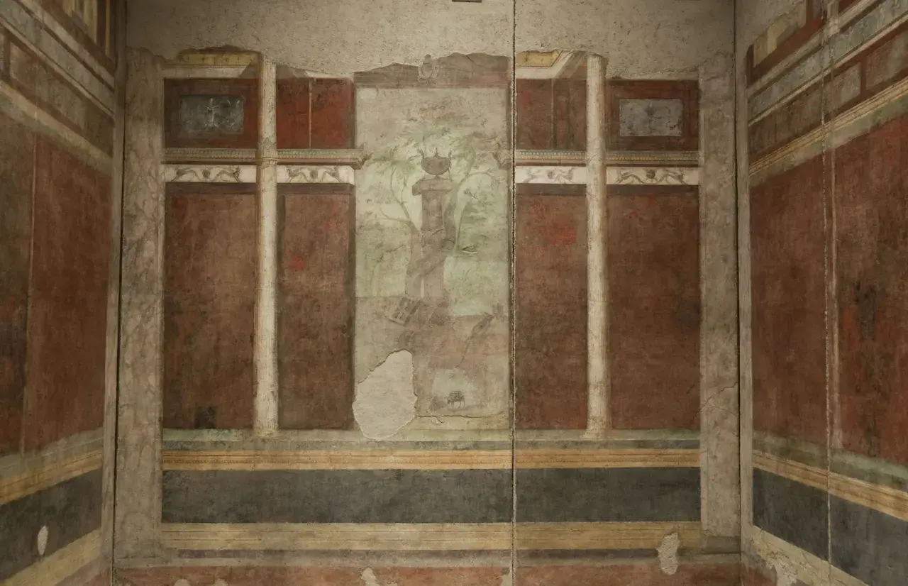 Affresco nella casa di Livia: colonne, pannelli rossi e un paesaggio centrale con un albero e un vaso.