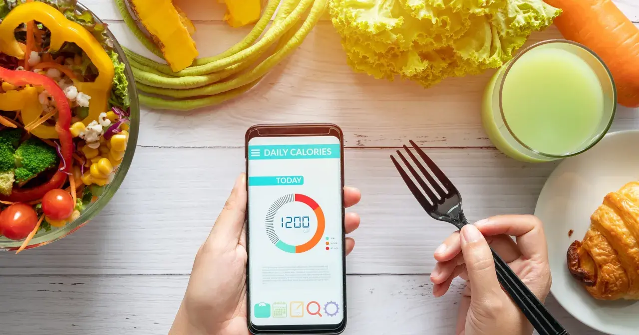 Aplikacja pokazuje dzienne zapotrzebowanie kaloryczne 1200 kcal. Obok sałatka, sok i rogalik.