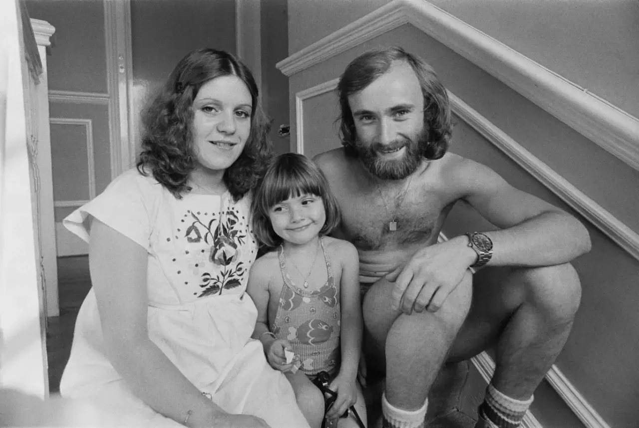 Phil Collins z żoną i córką, uśmiechnięci, siedzą na schodach.