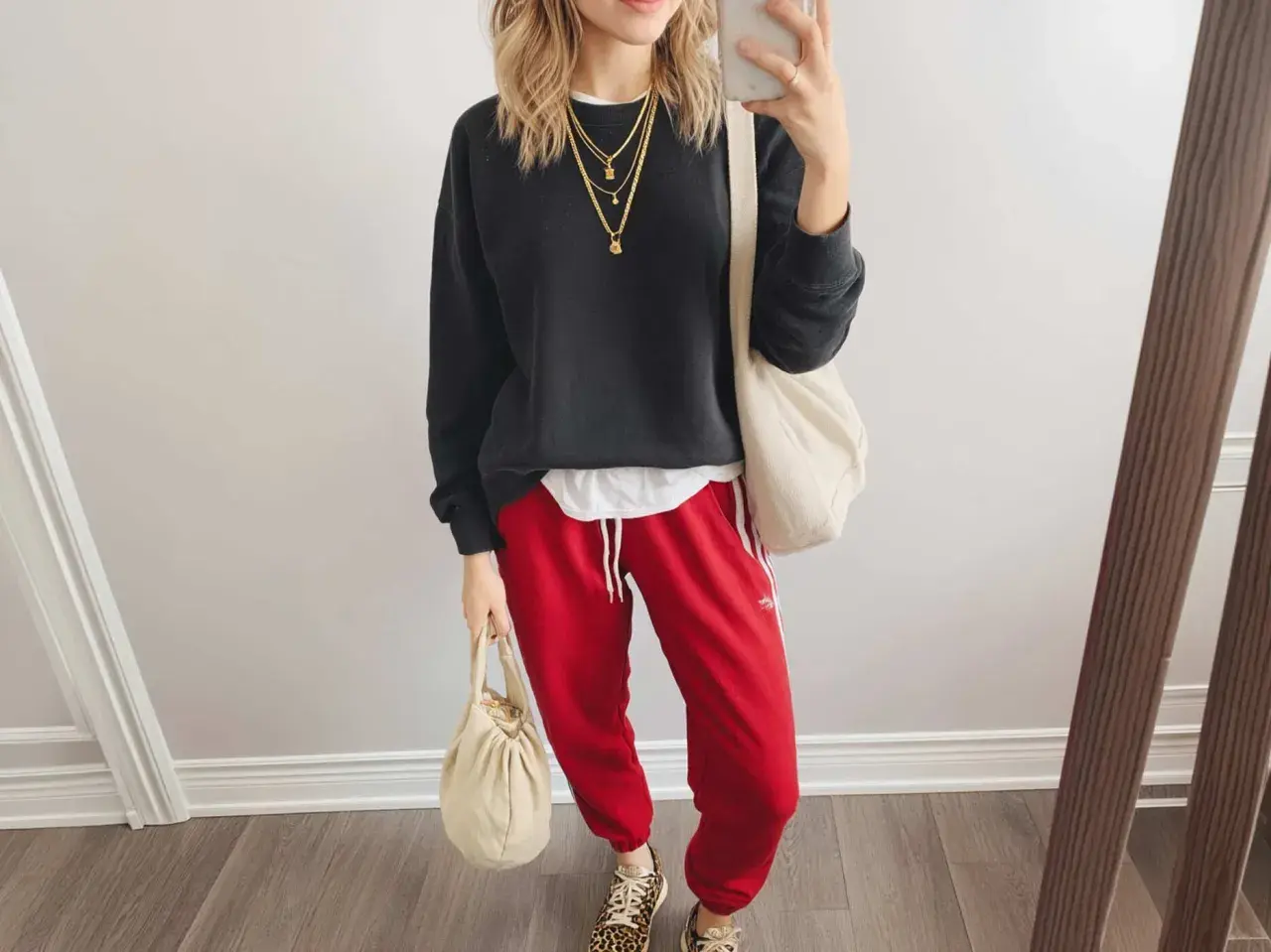 Styling-Idee: Schwarzer Pullover, weiße Schicht, rote Hose mit weißen Streifen, Leo-Sneaker und cremefarbene Taschen. Perfekt, wenn du fragst, was passt zu roter Hose!