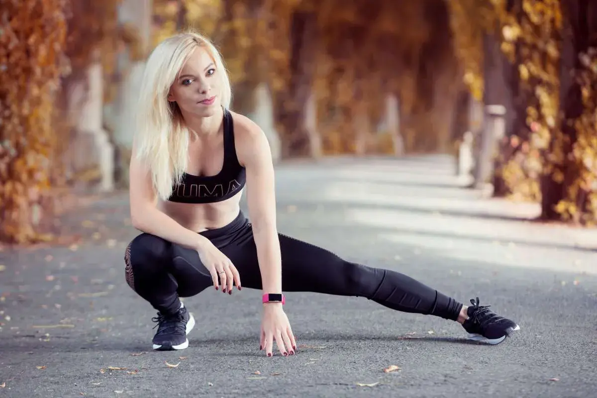 Blondynka w sportowym stroju wykonuje ćwiczenia rozciągające. Jej trening spinningowy jest gotowy do rozpoczęcia w jesiennej alei.