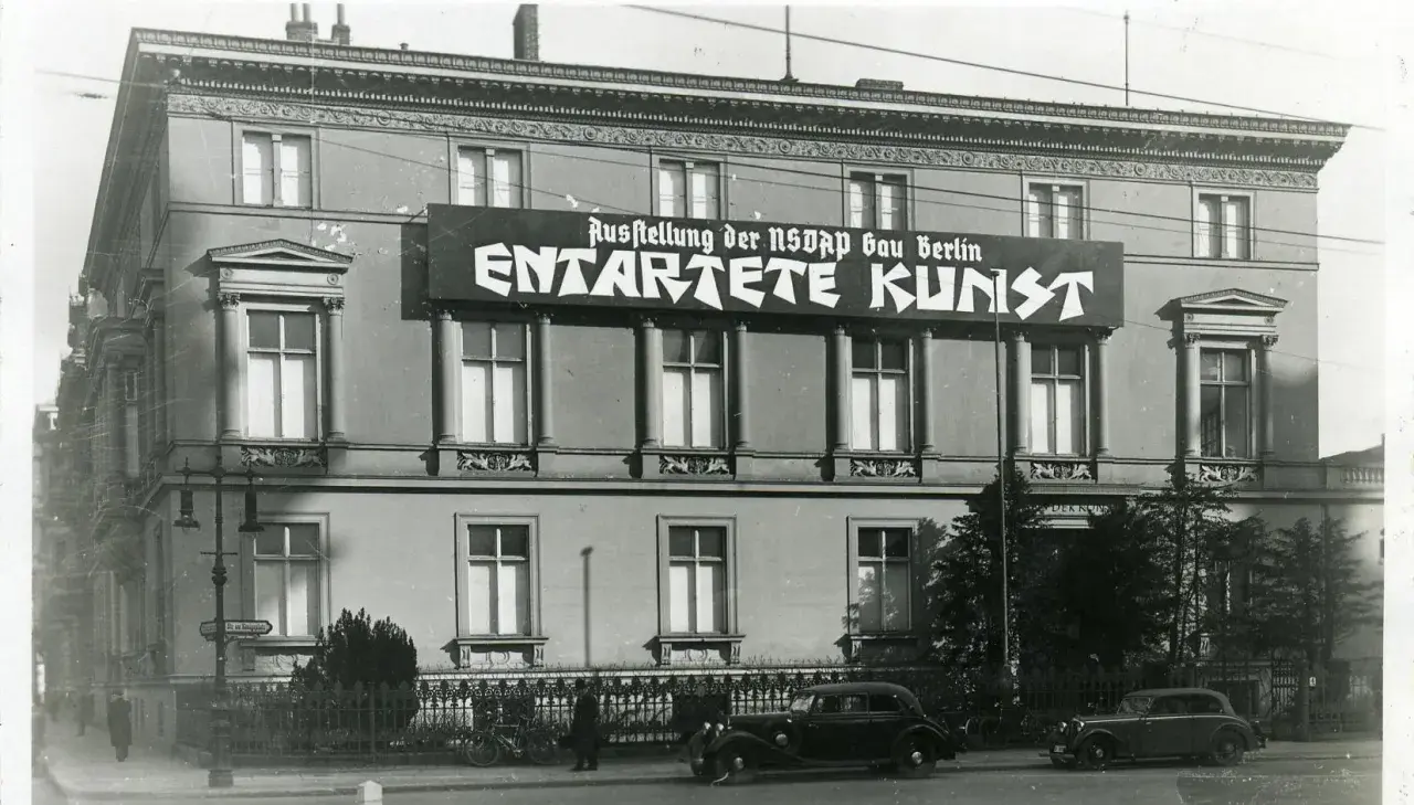 Große Banner verkünden die "Ausstellung der NSDAP Gau Berlin ENTTARTETE KUNST". Autos und Fahrräder stehen davor.