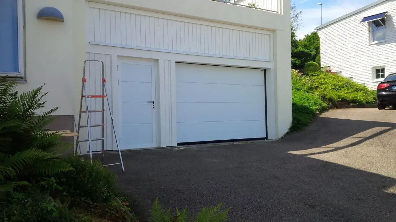 En vit garageport montering pågår. En stege står bredvid, redo för nästa steg.