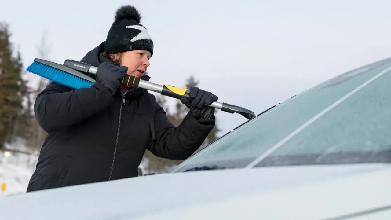 Kvinna skrapar is från bilruta med isskrapa. Kallstart bil kräver förberedelse.