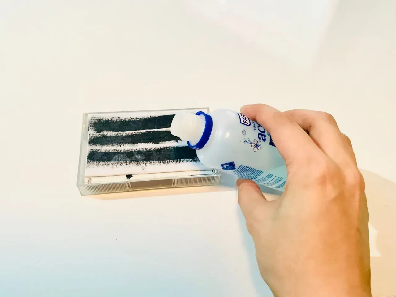 Mano versa liquido da flacone su nastro adesivo per rimuovere colla adesivi.