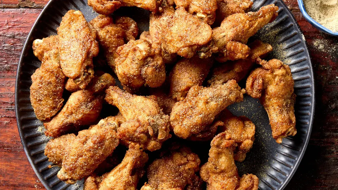 A pile of crispy, golden-brown Nagoya style chicken wings, seasoned with spices, on a dark plate.