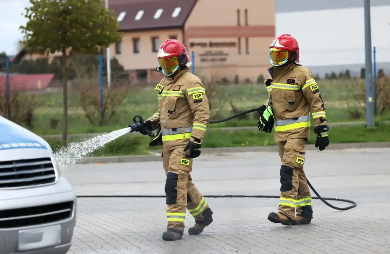 Strażacy w akcji, jeden z węża wodnego. Zastanawiasz się, ile zarabia strażak? To praca pełna poświęcenia.