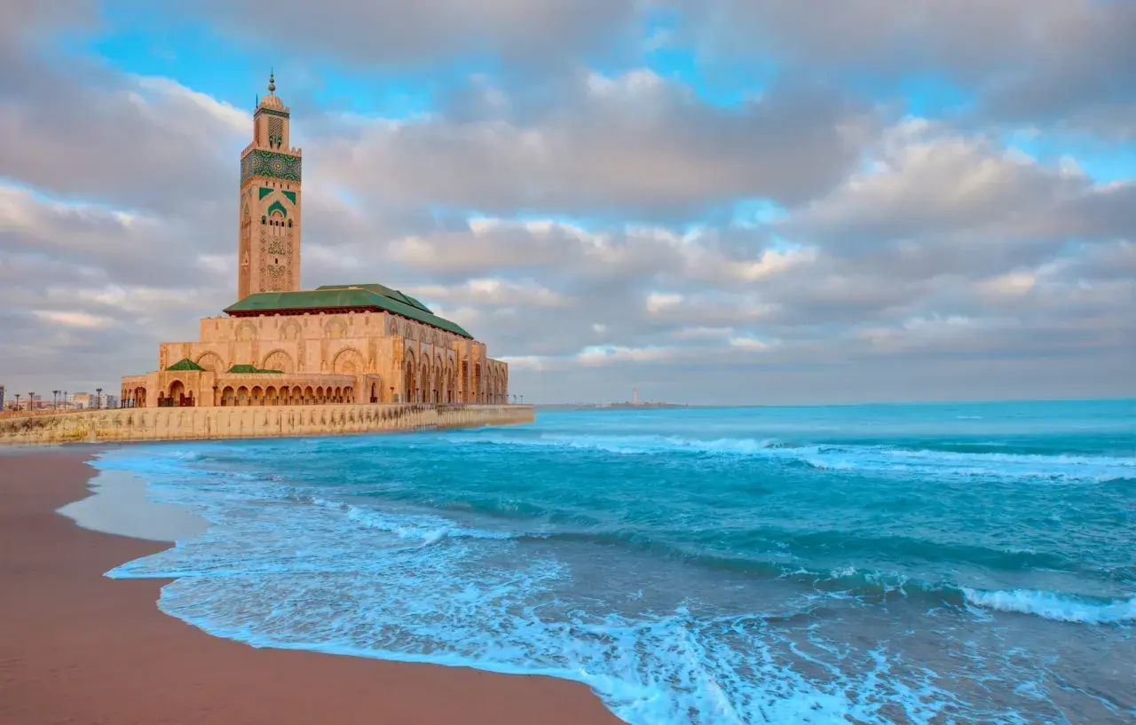 Wspaniałe maroko wakacje! Meczet Hassana II w Casablance nad turkusowym oceanem, z piaszczystą plażą i chmurami na niebie.
