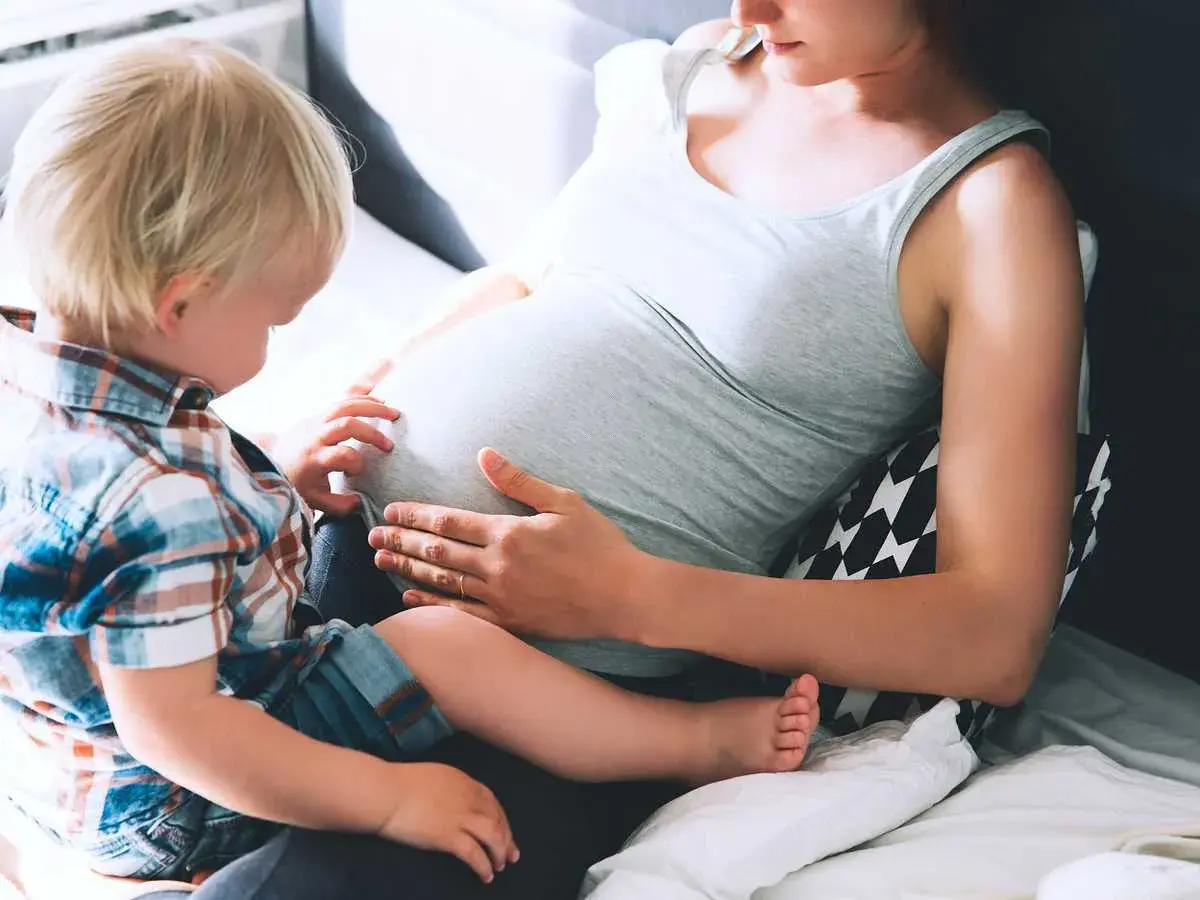 Liten pojke med blont hår känner på sin mammas mage, vecka 19.