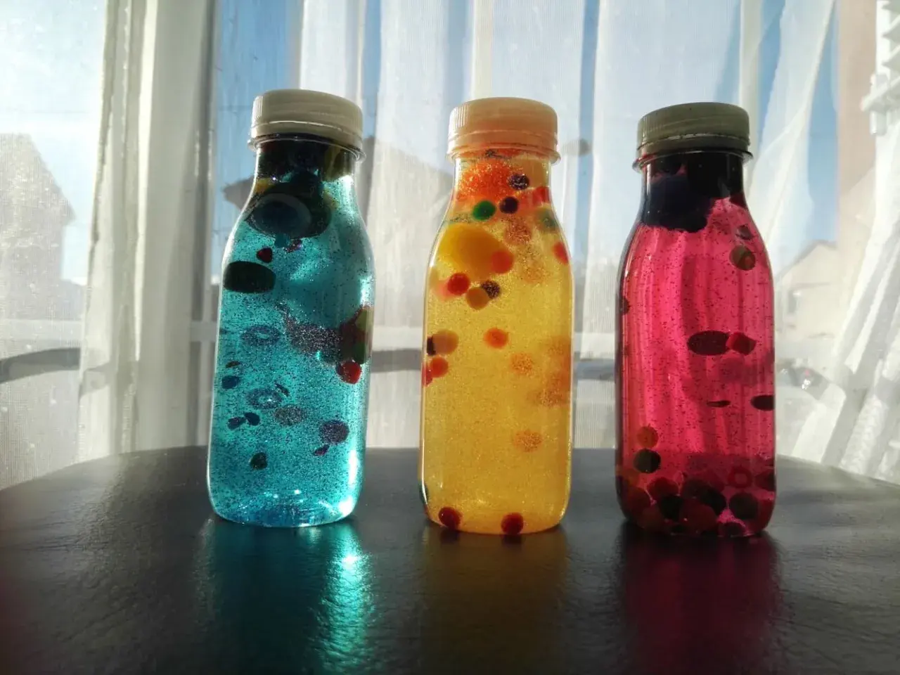 Tres botellas sensoriales caseras llenas de líquido brillante y bolitas de colores.