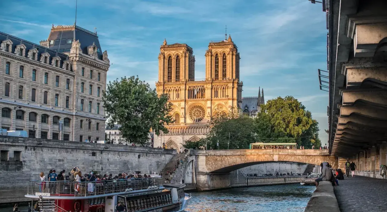 Katedra Notre Dame w Paryżu nad Sekwaną, z łodzią turystyczną i mostem w tle.