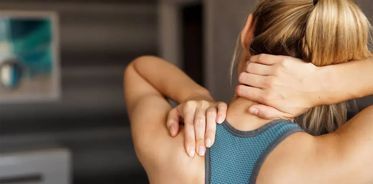 Une femme se masse le cou, peut-être pour soulager une douleur ou pour muscler son cou après un entraînement.