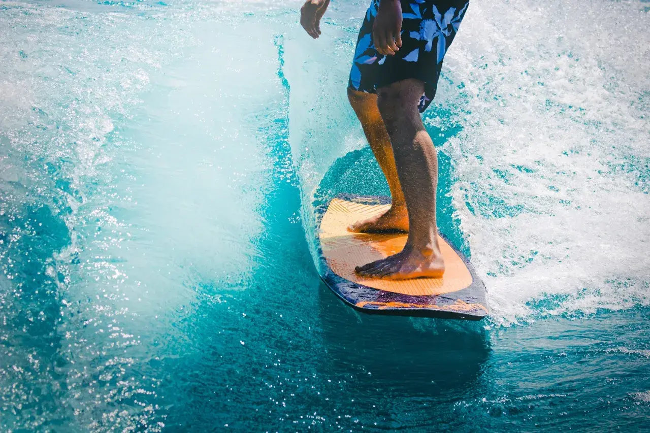Mężczyzna na desce surfingowej, czując orzeźwienie wody, jak po użyciu perfum allure homme sport.