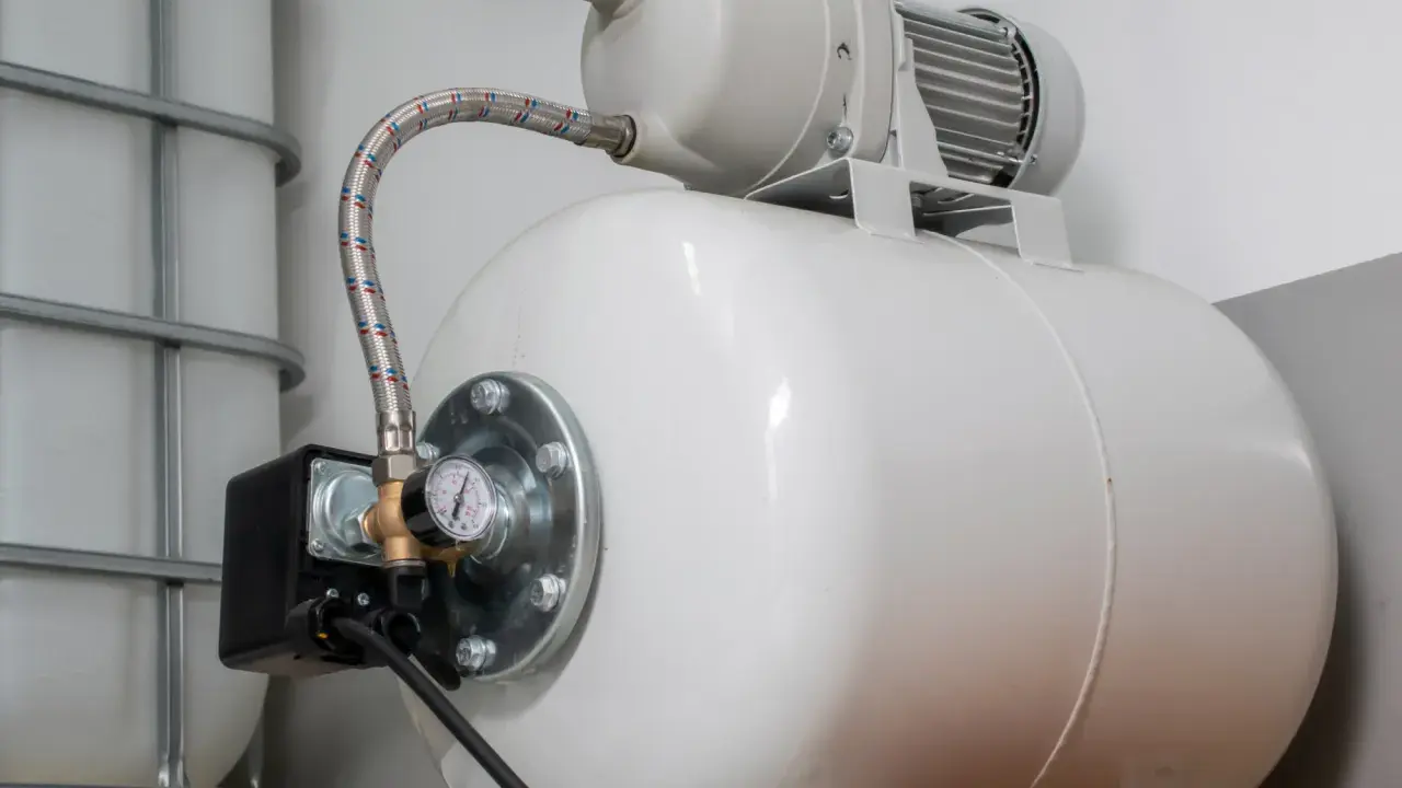 Biały zbiornik hydroforowy z manometrem i wężem. Może to oznaczać, że hydrofor często się włącza.