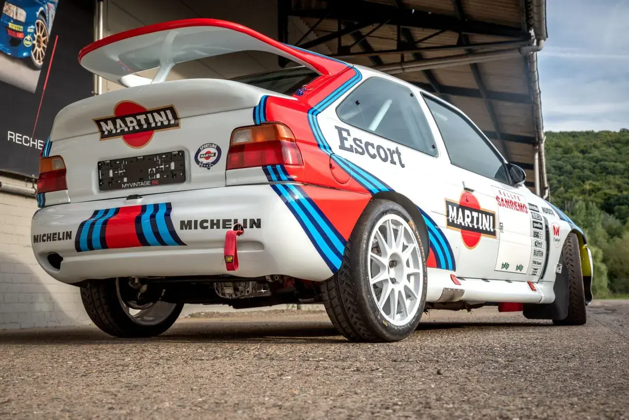 Biały Ford Escort Cosworth w barwach Martini Racing, z dużym tylnym spojlerem i licznymi naklejkami sponsorów.