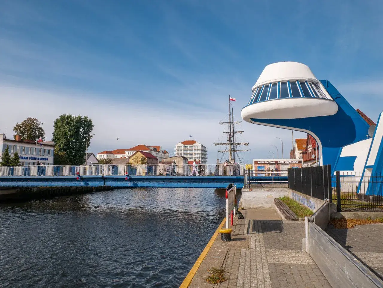 Niebieski most nad Regą w malowniczym mieście. W tle żaglowiec i nowoczesna architektura.