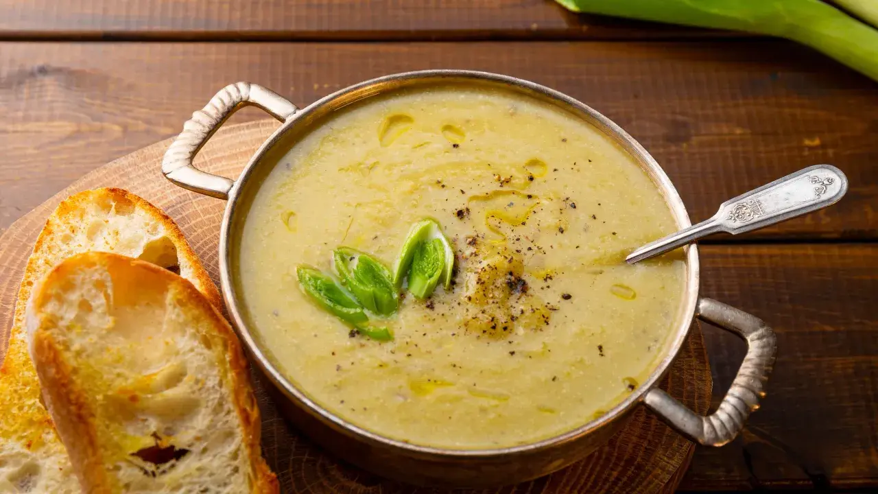 Una ciotola di calda crema di patate, guarnita con cipollotto fresco e pepe nero, servita con fette di pane tostato.