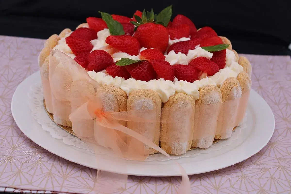 Charlotte aux fraises et fromage blanc, décorée de crème fouettée et de menthe fraîche. Un ruban pêche enlace le pourtour de biscuits à la cuillère.