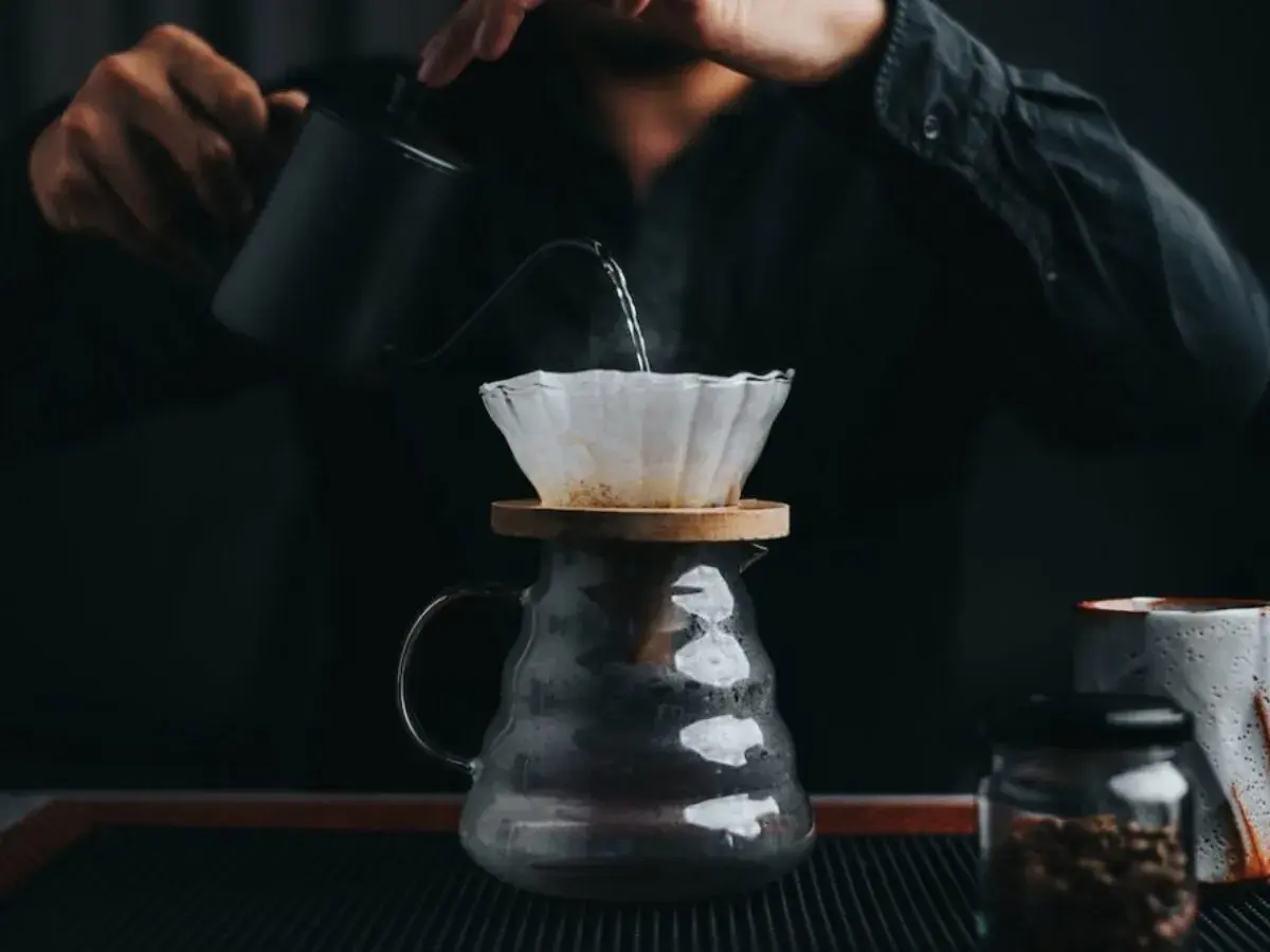 En person häller varmt vatten över kaffefilter för att brygga dropp kaffe. Ånga stiger från den nybryggda drycken.