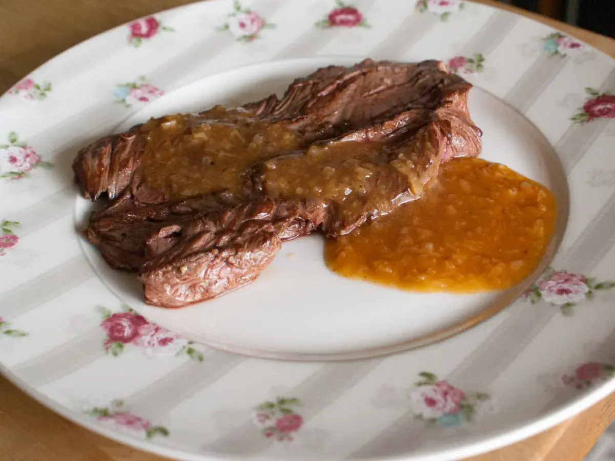 Un plat de viande tendre nappé d'une sauce onctueuse à l'échalote, servi sur une assiette à motifs floraux.