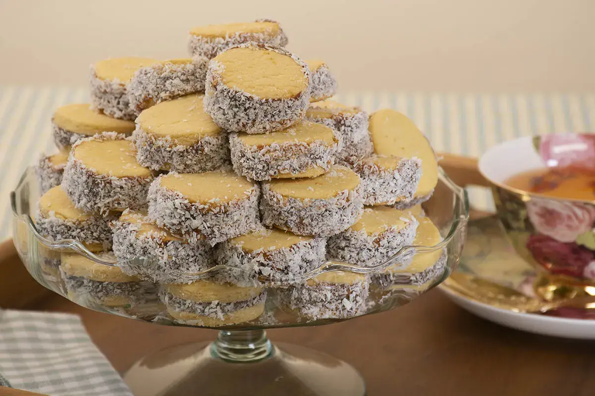 Montón de alfajores de maicena cubiertos de coco rallado, apilados en una fuente de vidrio.