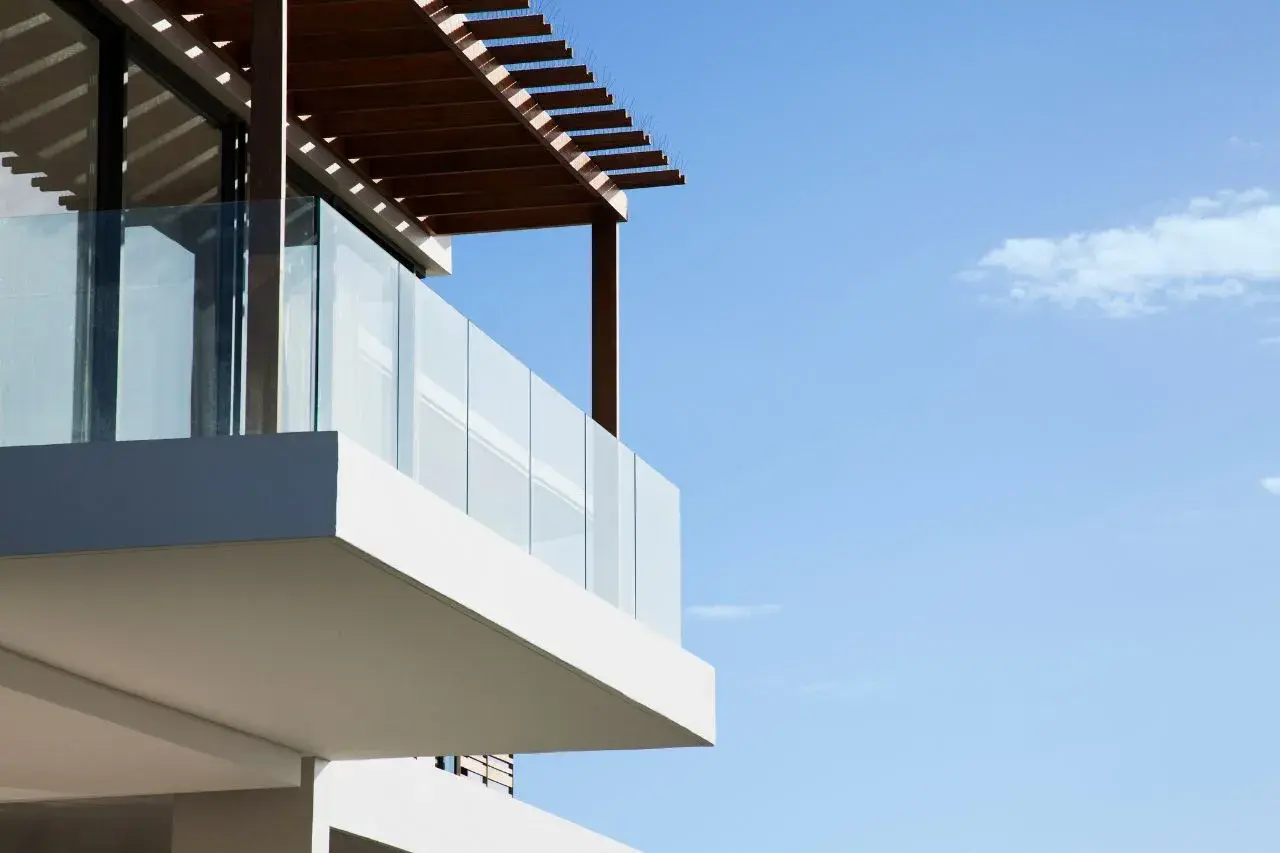 Nowoczesny balkon z przeszkloną balustradą i drewnianą pergolą to świetny pomysł, czym osłonić balkon, zapewniając prywatność i cień.