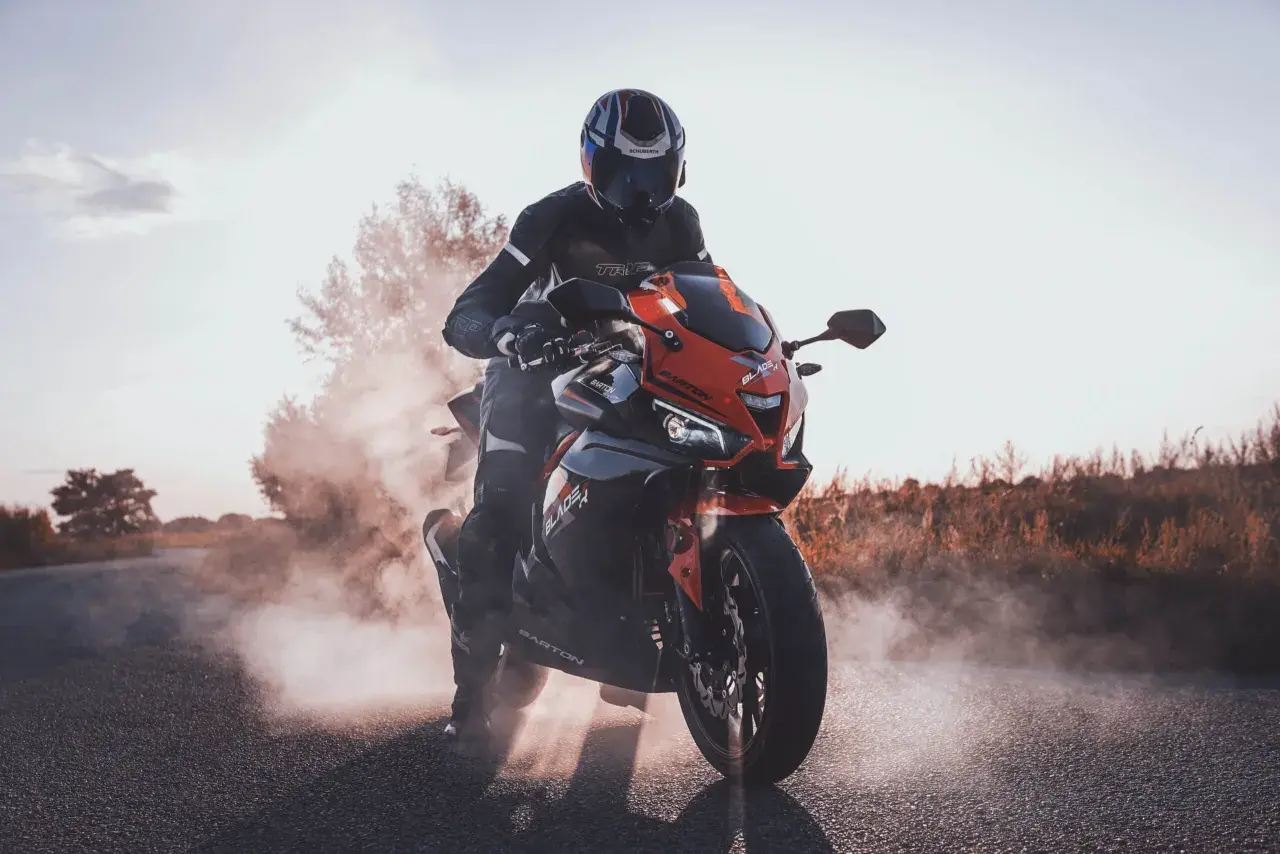 Motocyklista w kasku i kombinezonie na czerwono-czarnym motocyklu Barton Blade 125, unoszący kurz. Czy motocyklem 125 można jeździć po autostradzie?